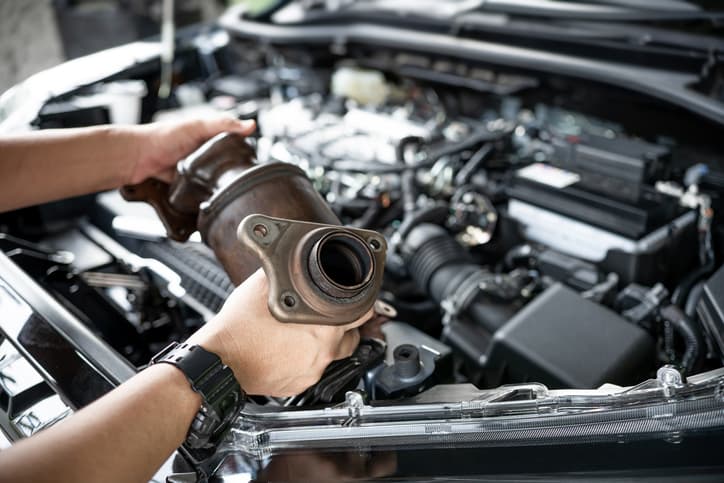 Mechaniker hält Katalysator im Motorraum